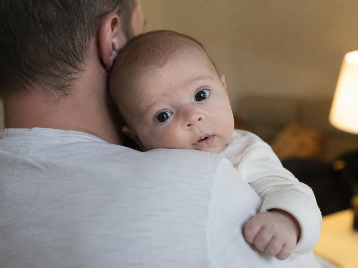 Bebis på 3 månader som ler i föräldrarnas armar under familjefotografering